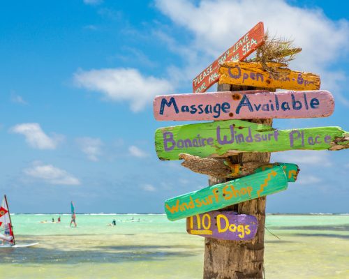 Colorful,Signpost,At,Coast,Of,Bonaire,With,Windsurfers,On,Sea