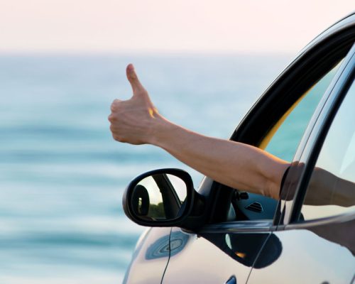 Man,Showing,Thumbs,Up,From,Car,Window,With,Sea,And